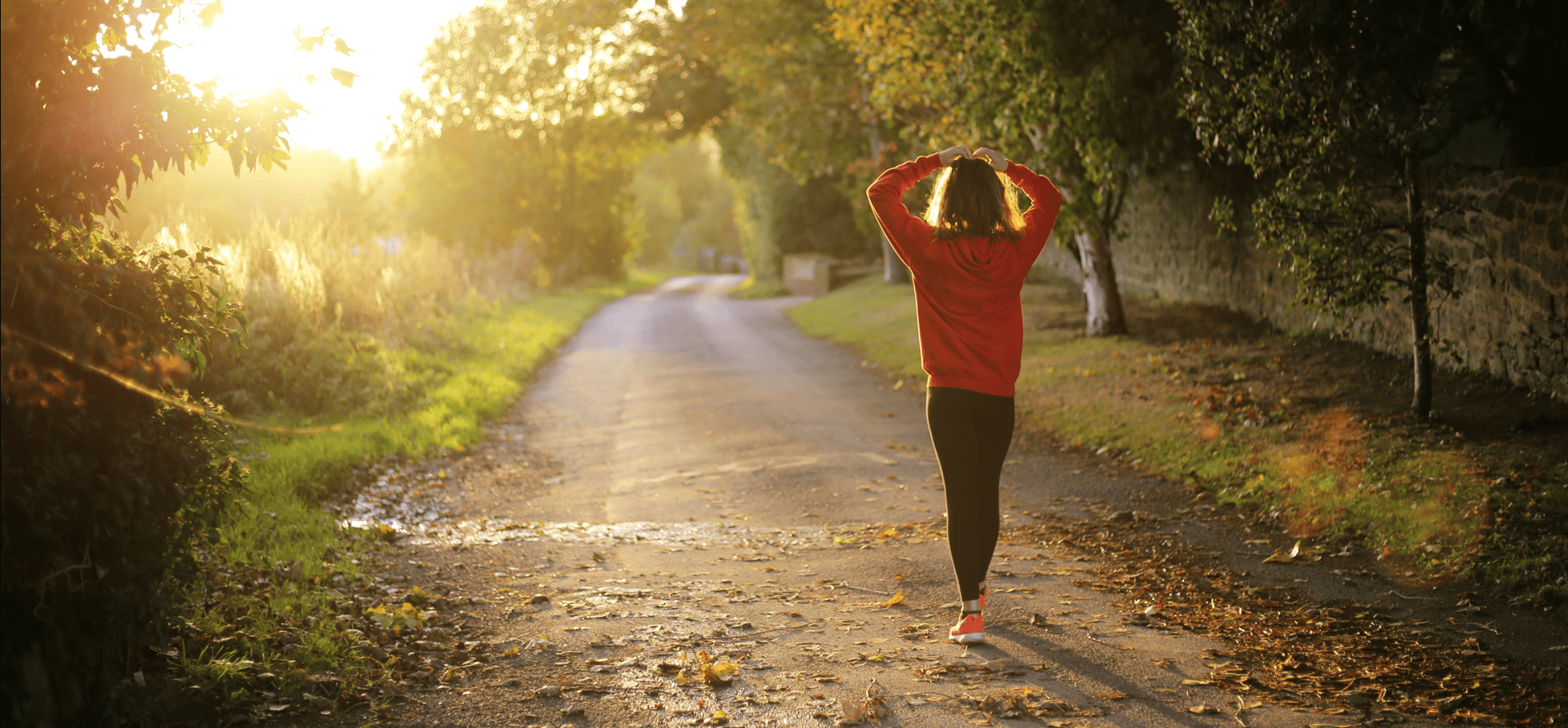 Young woman in athletic gear walking along a path during an autumn sunset